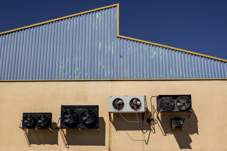 Exterior view of industrial air conditioning units mounted on a warehouse wall under clear blue sky.